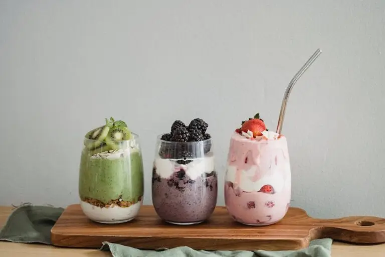 Colorful homemade fruit smoothies with kiwi, blackberry, and strawberry on a wooden board.